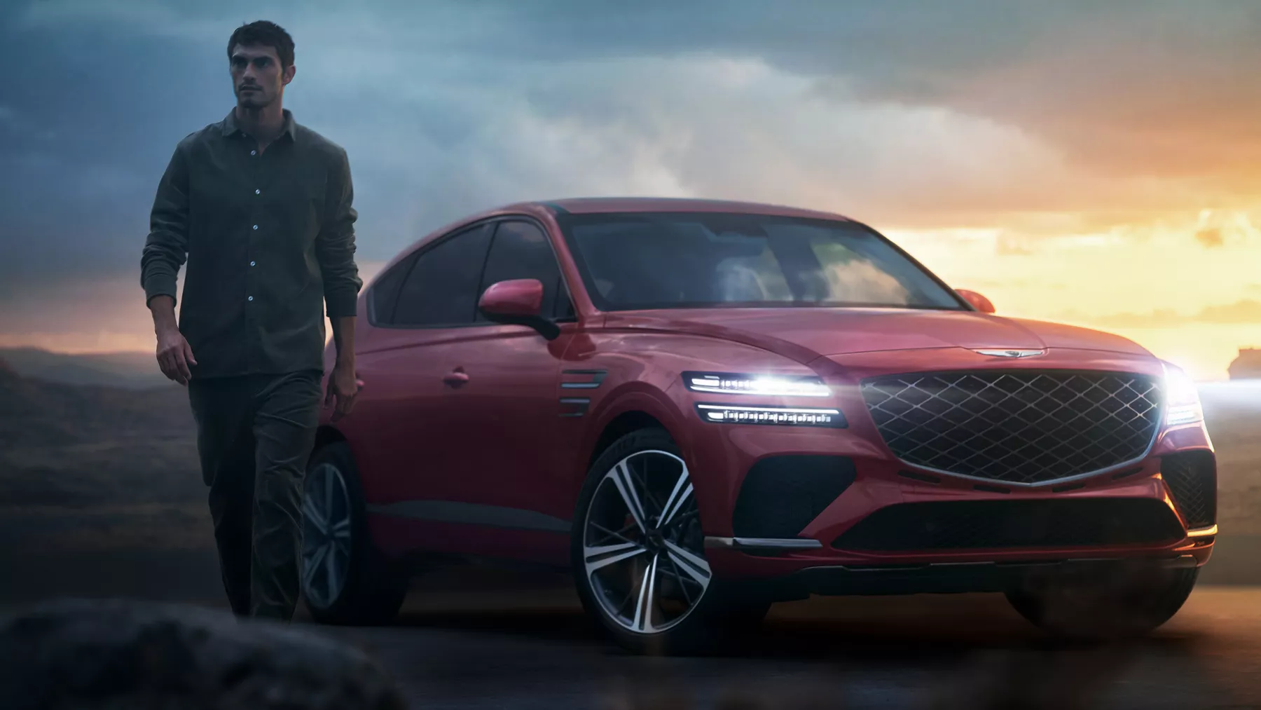 Man walking beside GV80 Coupe with headlights illuminated.