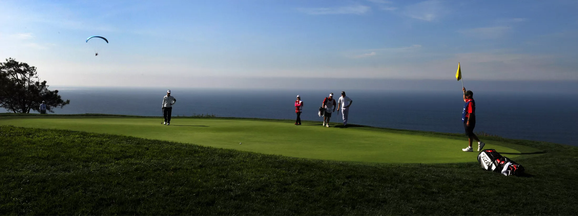 Golfers on the green at Torrey Pines with parachutists in the sky at Genesis Invitational