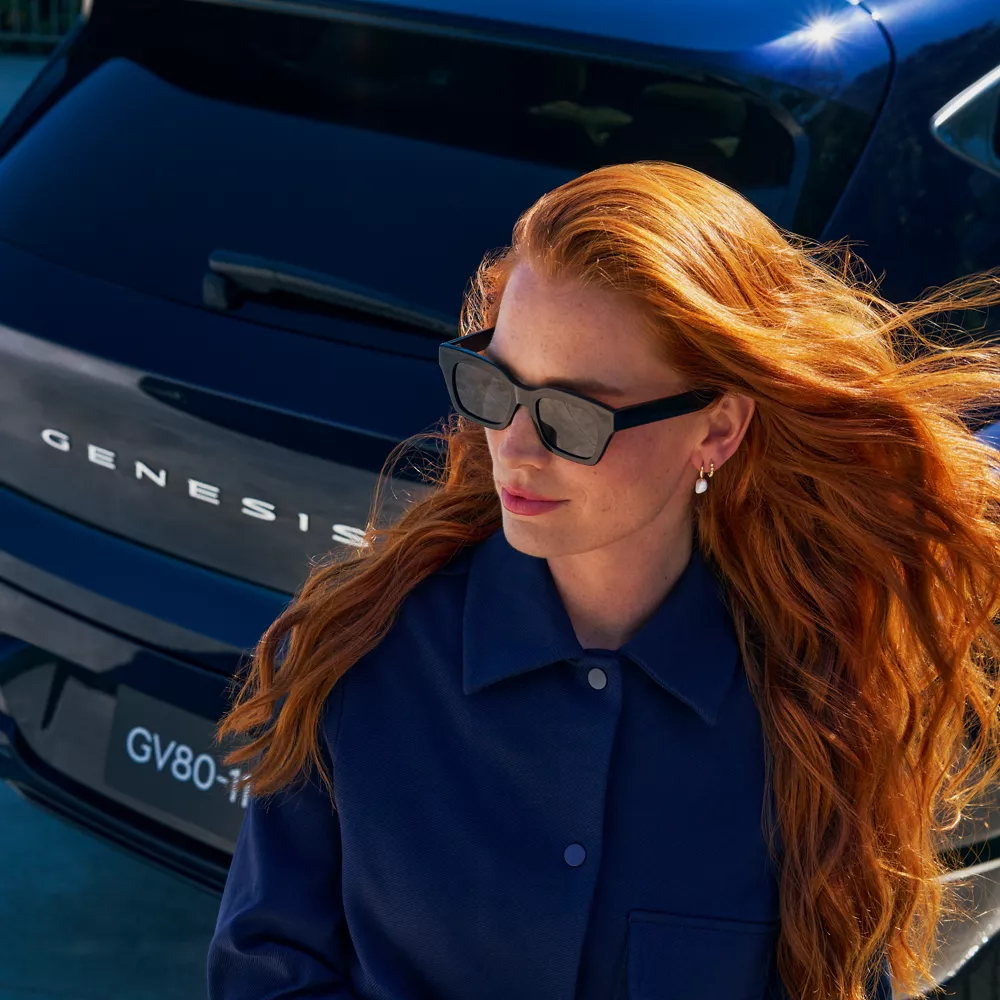 A female with red hair walking past a parked GV80.