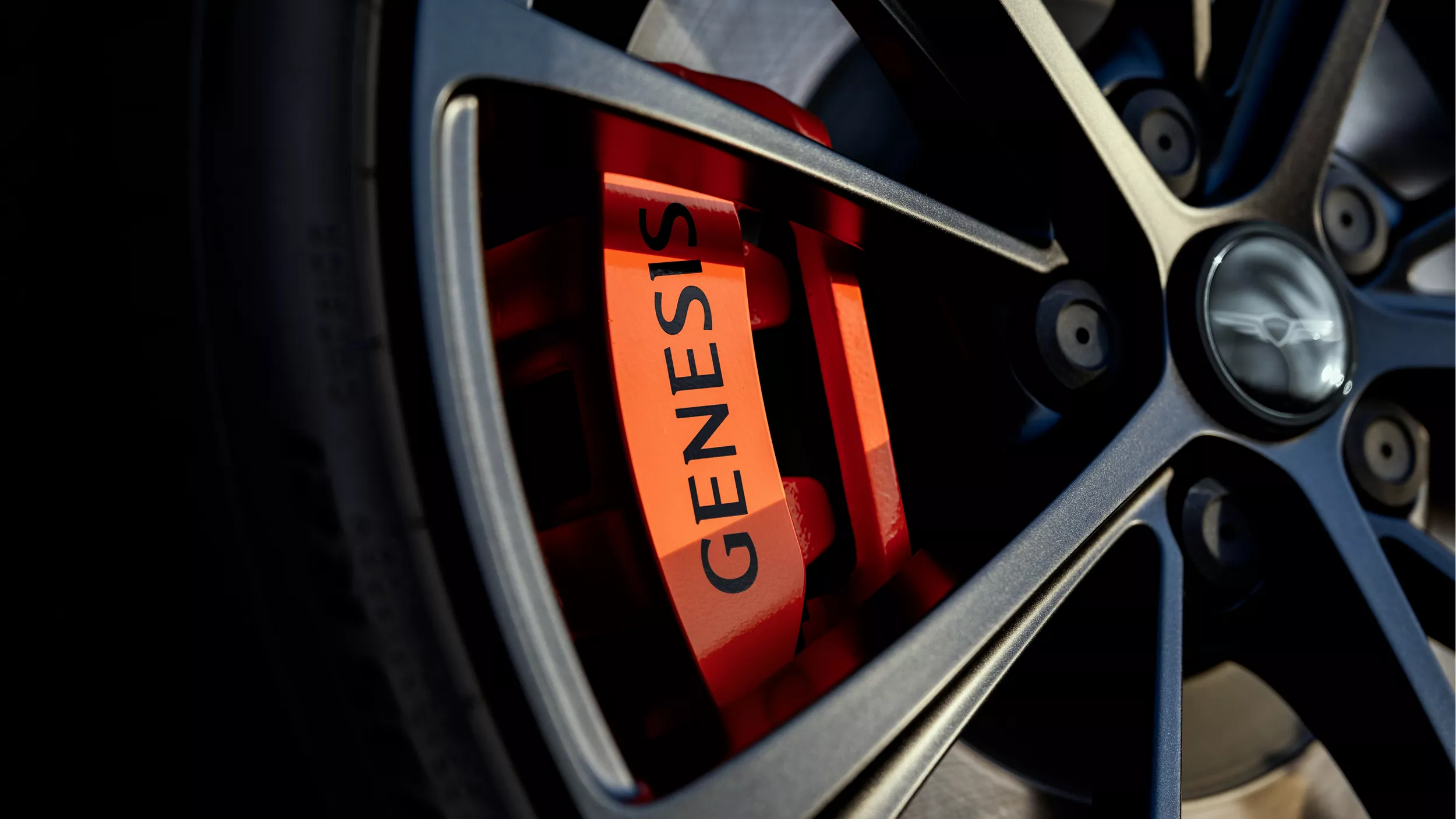Close-up of alloy wheel with orange brake caliper featuring "Genesis" in black lettering