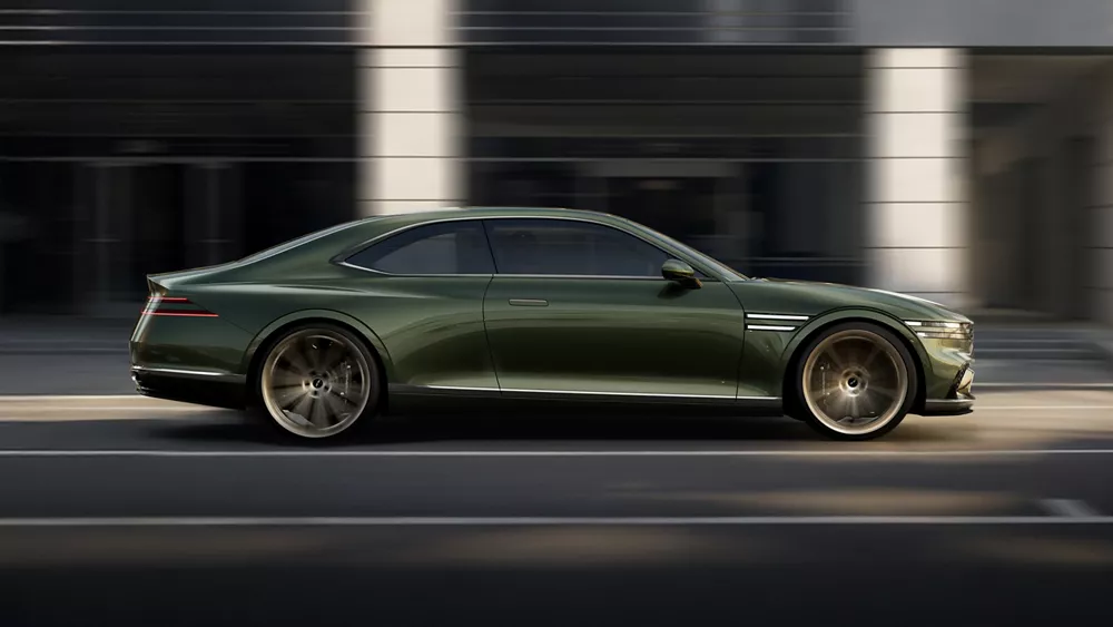 Passenger side profile of green Genesis X Gran Coupe Concept vehicle in motion on city street