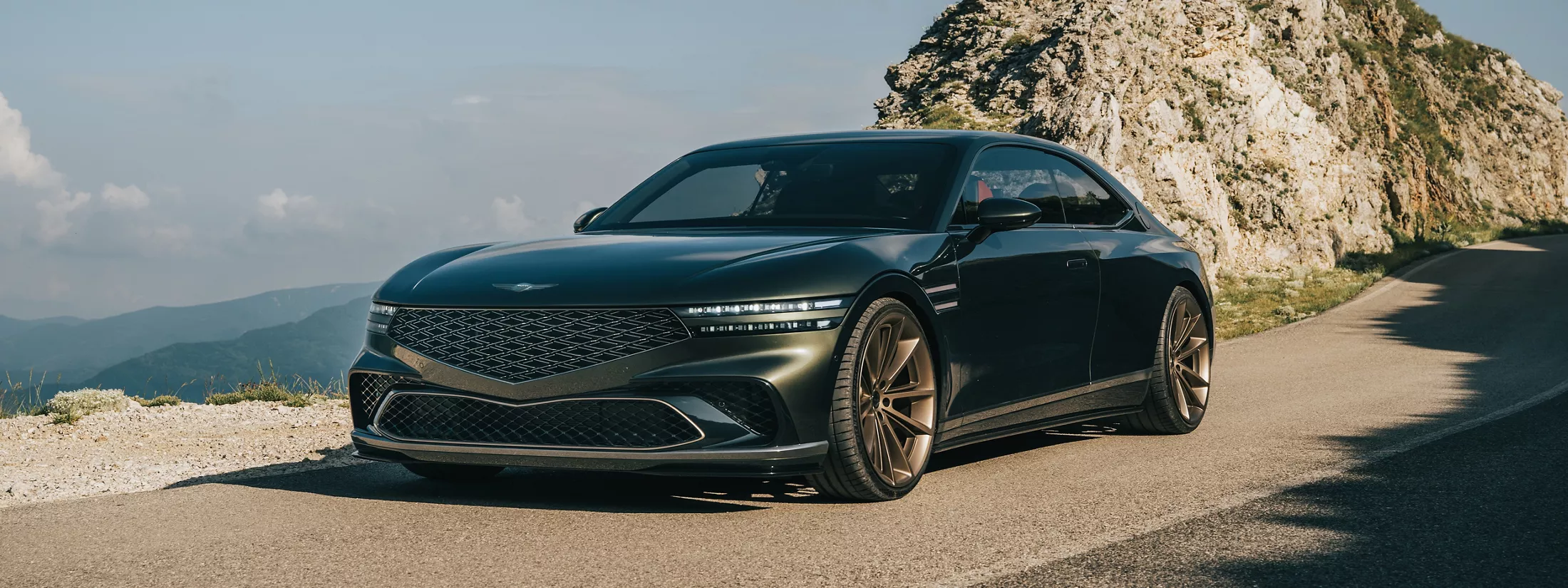 3/4 front driver side angle of X Gran Coupe Concept vehicle driving down mountainous road by a cliff