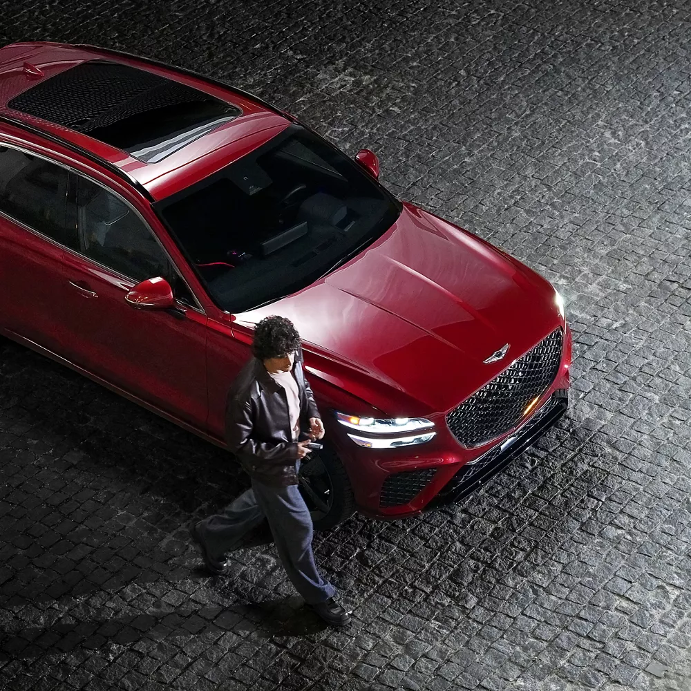 Aerial view of a man walking past a red Genesis GV70 SUV