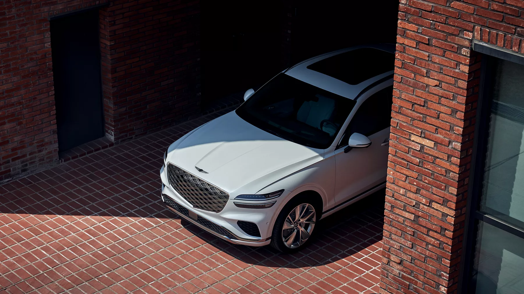 Aerial shot showing the front half of a white 2026 GV70 parked in a driveway