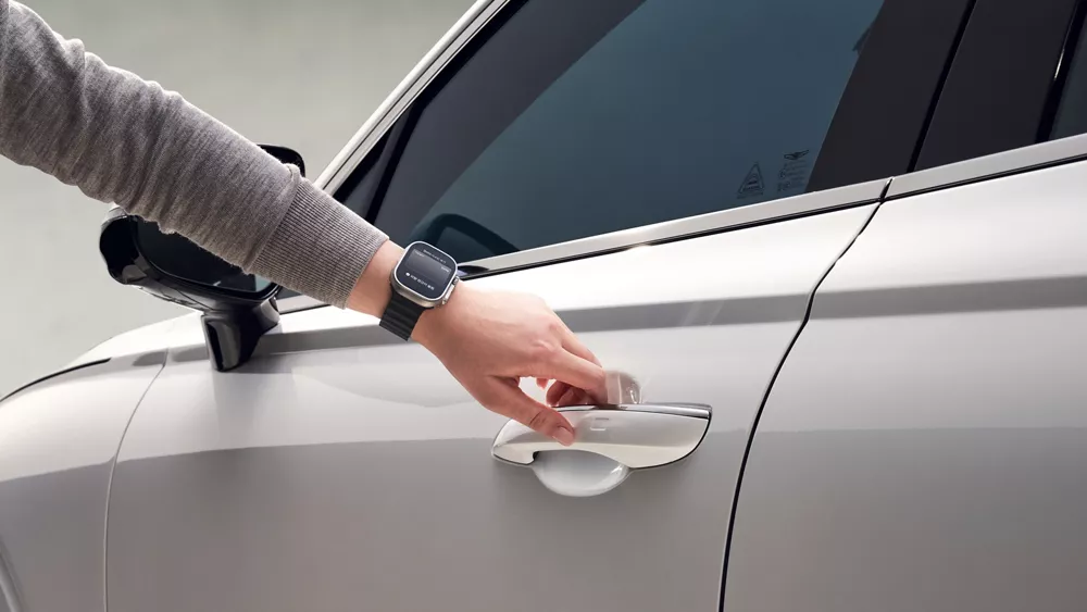 Close up of a person reaching to grasp the driver side door handle on white 2026 GV70