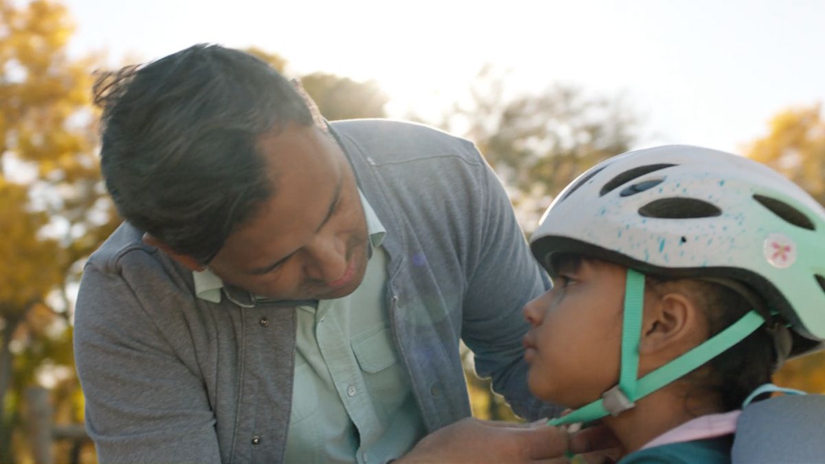 Conductores felices de Hyundai: Un padre ayuda a su hijo a ajustarse el casco de bicicleta.