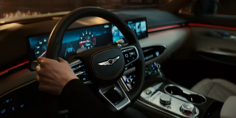 Interior close-up of driver holding Genesis GV70 steering wheel, with robotic light bulbs outside