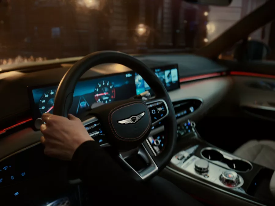 Interior close-up of driver holding Genesis GV70 steering wheel, with robotic light bulbs outside