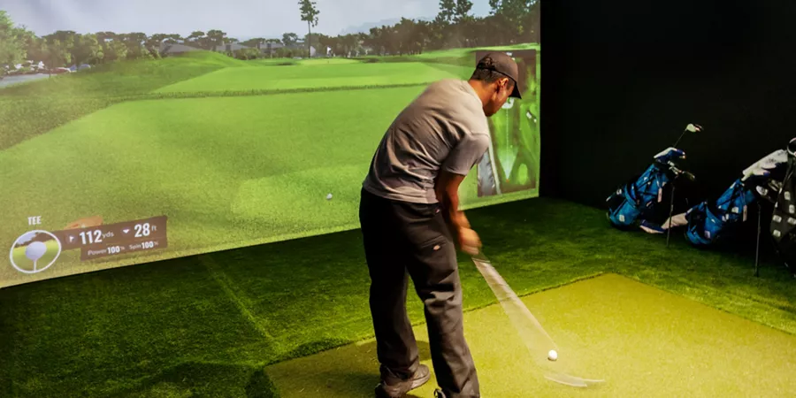 Person mid-swing on an indoor golf simulator at a Genesis Golf Invitational Lounge