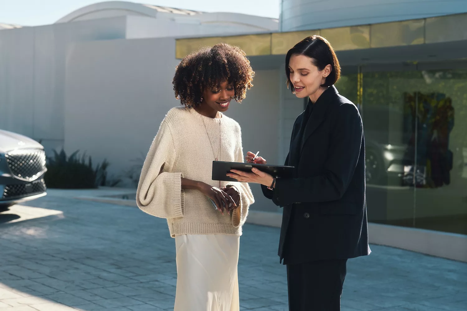 Genesis concierge using tablet while speaking to customer as both stand in front of modern home