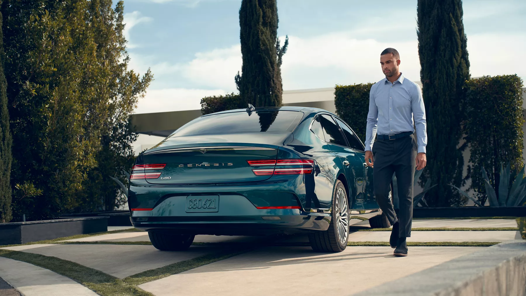 Rear view of Genesis Electrified G80 in Matira Blue parked on driveway as man walks along side