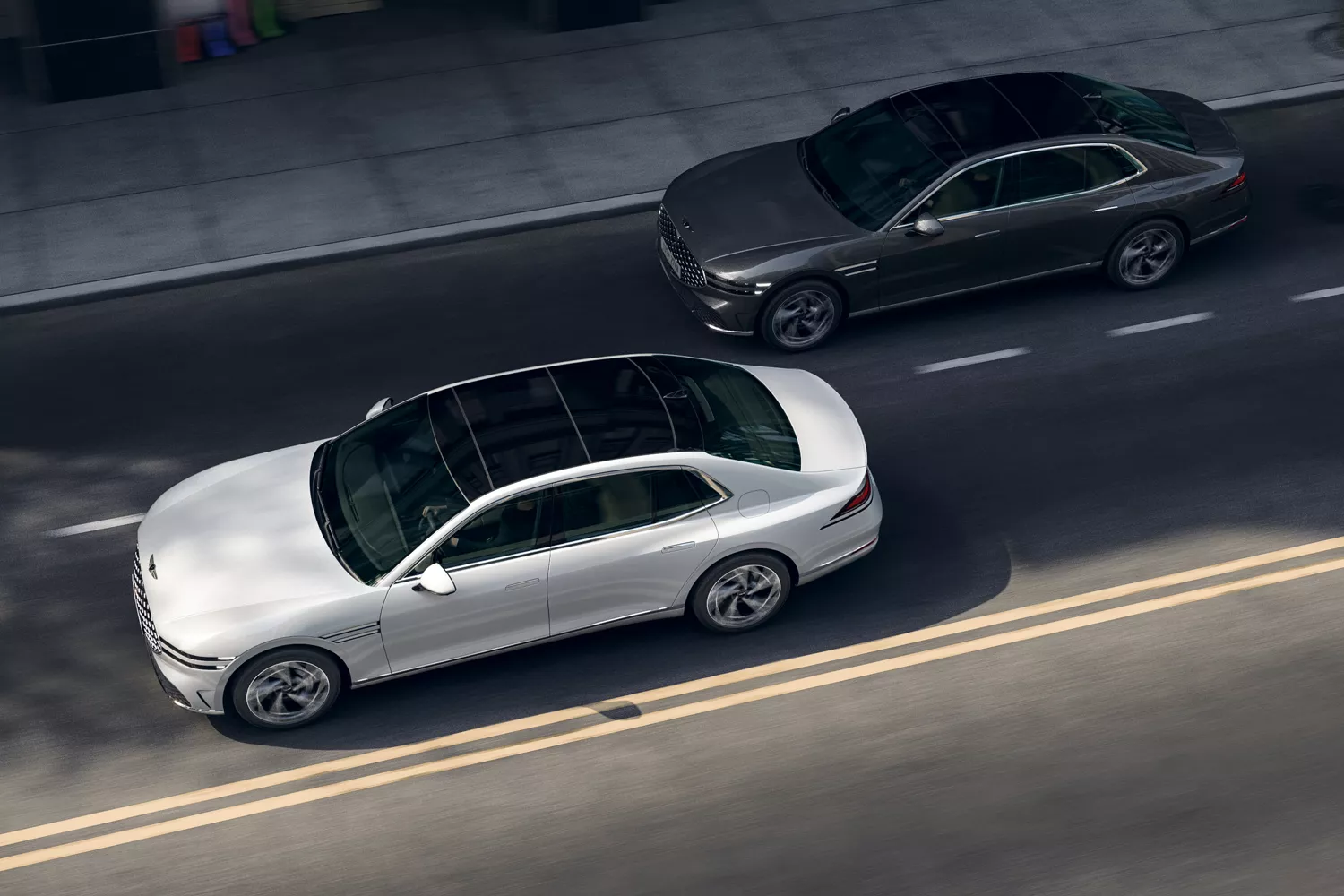 Aerial view of Genesis G90 sedans in Makalu Gray and Uyuni White drive side by side on a city street
