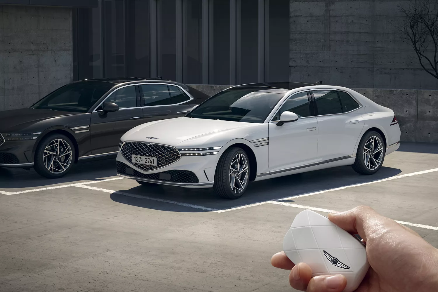 Hand holding Genesis Key Fob in front of black and white Genesis G90 sedans parked side by side