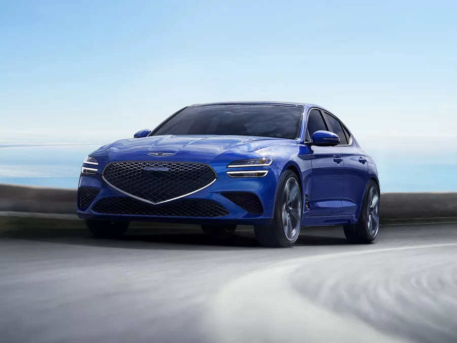 Front driver side action shot of Genesis G70 in Kawah Blue driving on a coastal highway