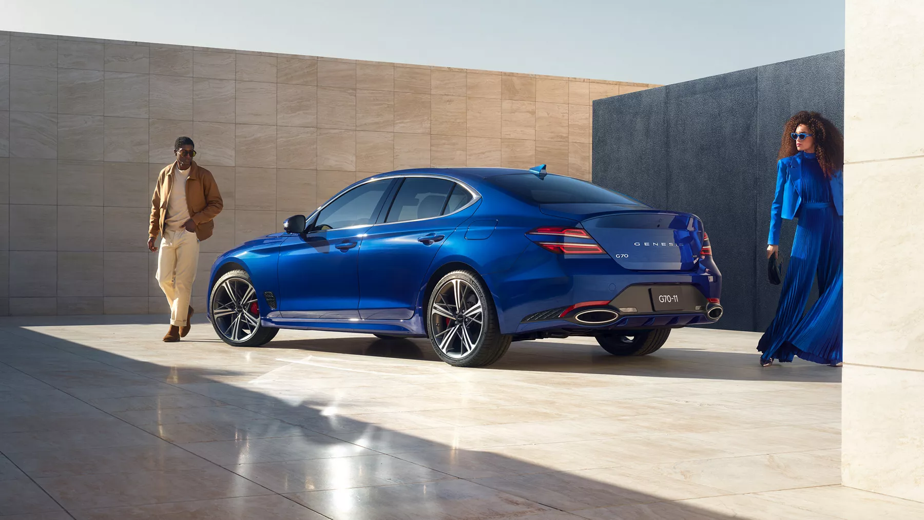 一褐衣男子與一藍衣女子雙雙近距站在車旁所見 Genesis G70 (Kawah Blue) 駕駛側後視照