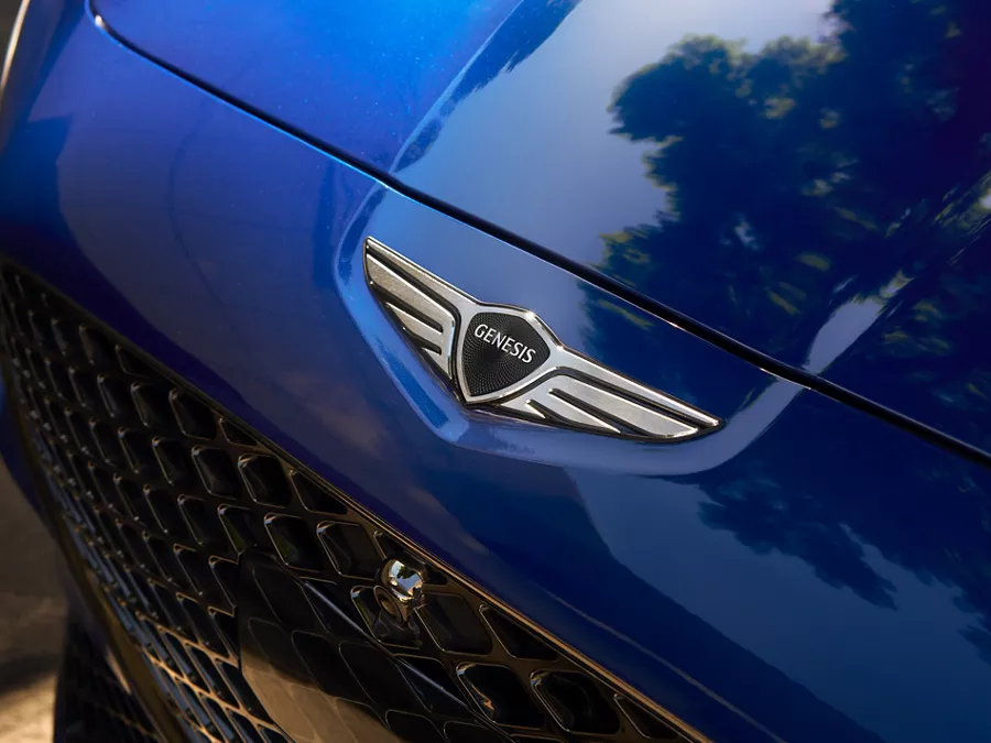 Close up overhead shot of Genesis emblem logo on the hood of a Genesis G70 in Kawah Blue