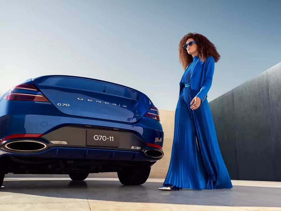 Rear view of Genesis G70 in Kawah Blue as woman dressed in blue walks behind parked vehicle