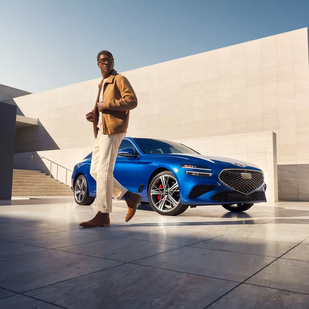 Genesis G70 (Kawah Blue) 停在頂層上有一男子走在車前的乘客側視角照