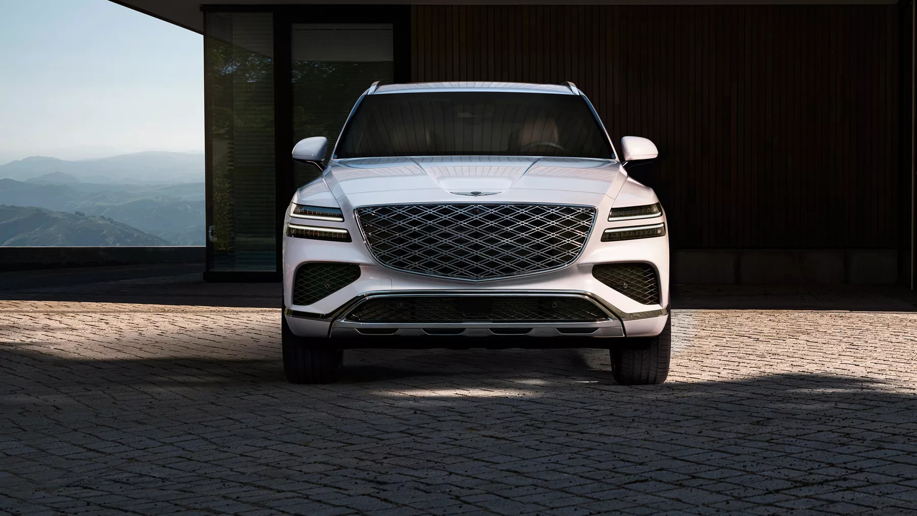 Front view of Uyuni White Genesis GV80 SUV on cobblestone driveway with scenic mountain backdrop
