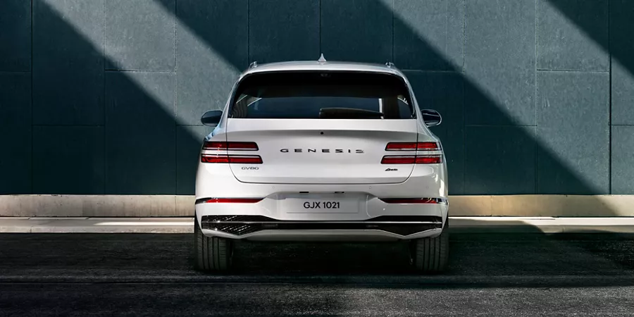 Rear view of white Genesis GV80 parked in front of cement building