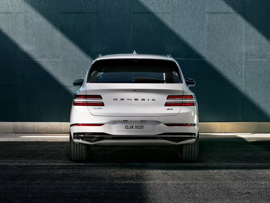 Rear view of white Genesis GV80 parked in front of cement building