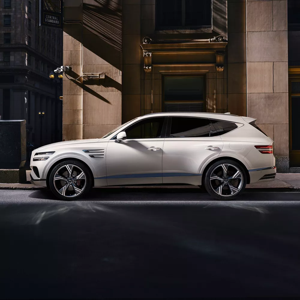 Driver's side profile view of Genesis GV80 in white parked on a city street