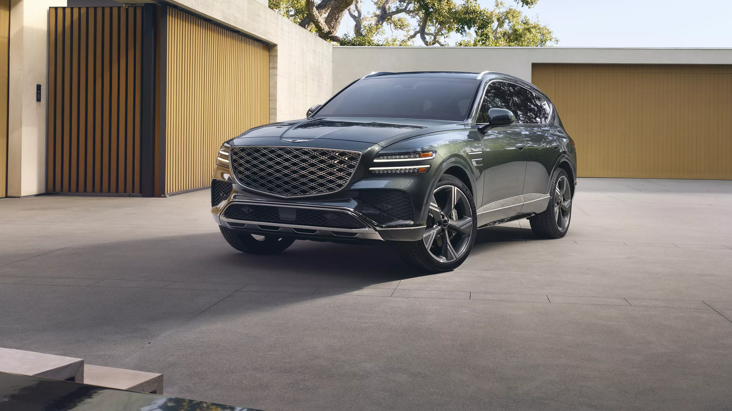 3/4 front driver side view of Genesis GV80 3.5T Prestige AWD parked in driveway of modern house