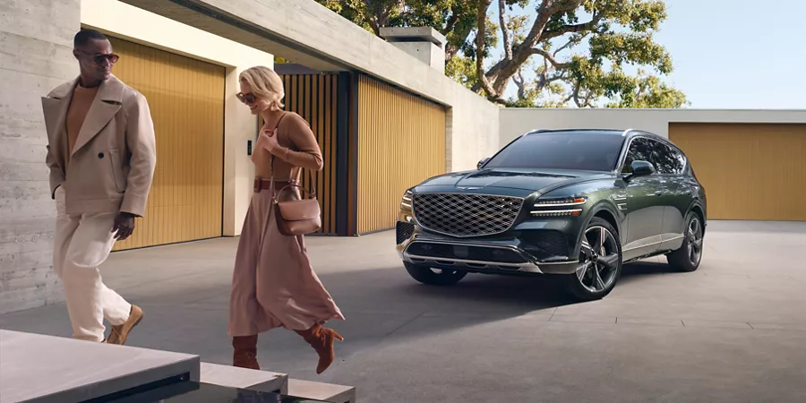 Front driver side view of Genesis GV80 luxury SUV on modern driveway with two people walking by