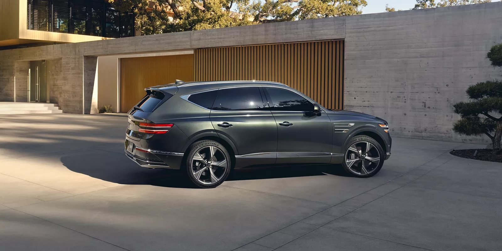 Passenger side profile view of Genesis GV80 in Storr Green parked by modern house