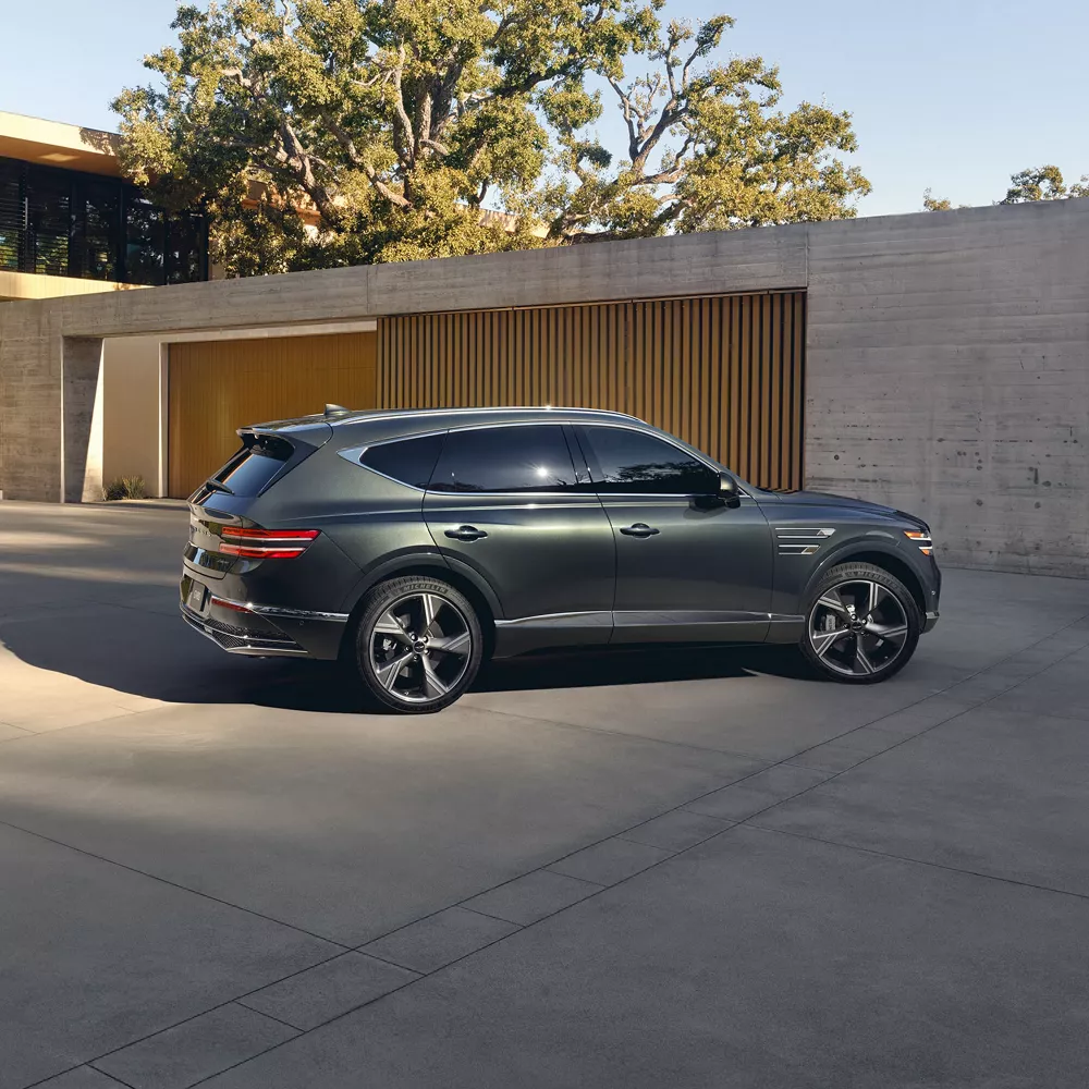 Passenger side profile view of Genesis GV80 in Storr Green parked by modern house