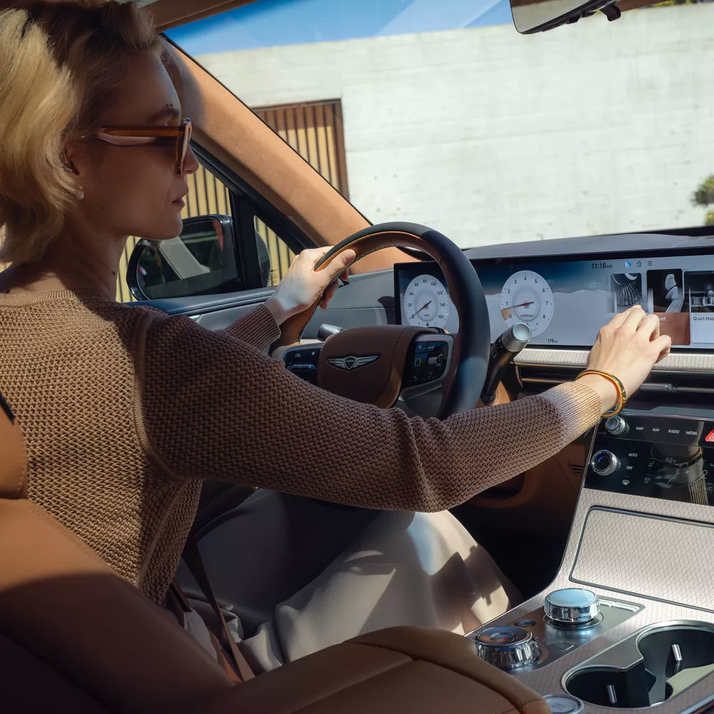 Interior backseat view of driver inside Genesis GV80 with tan leather seating using OLED display