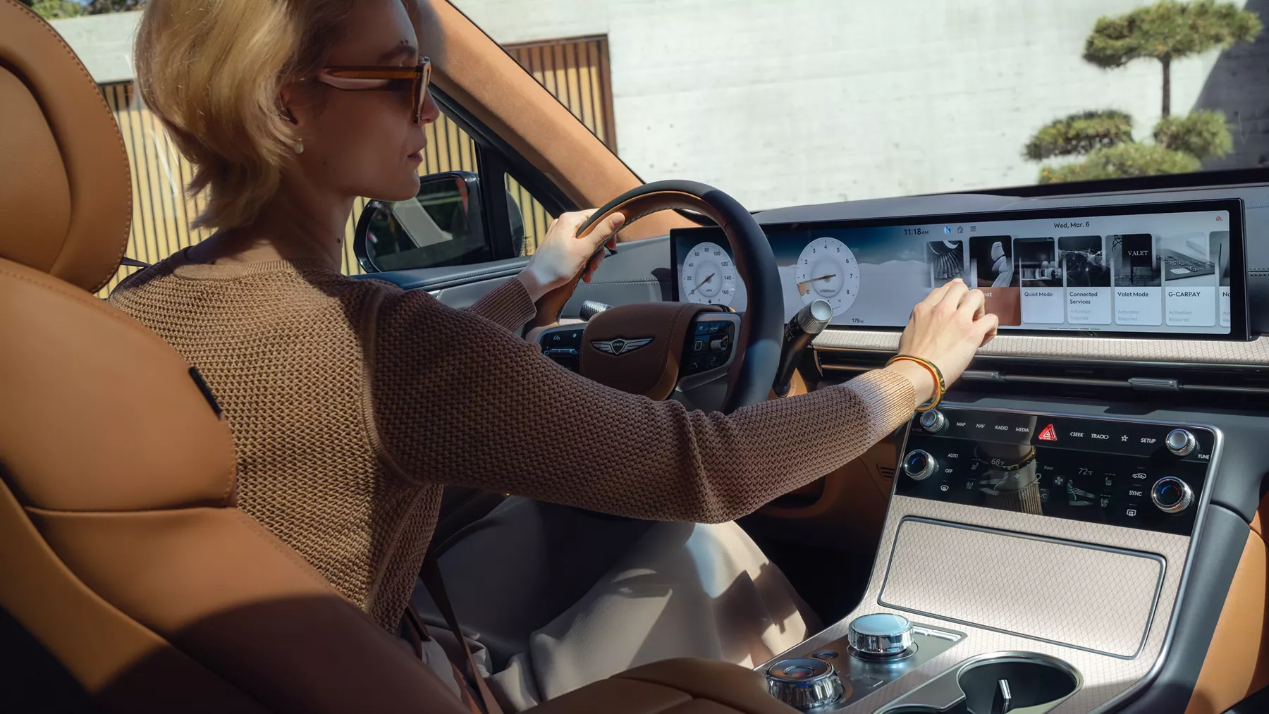 Interior backseat view of driver inside Genesis GV80 with tan leather seating using OLED display
