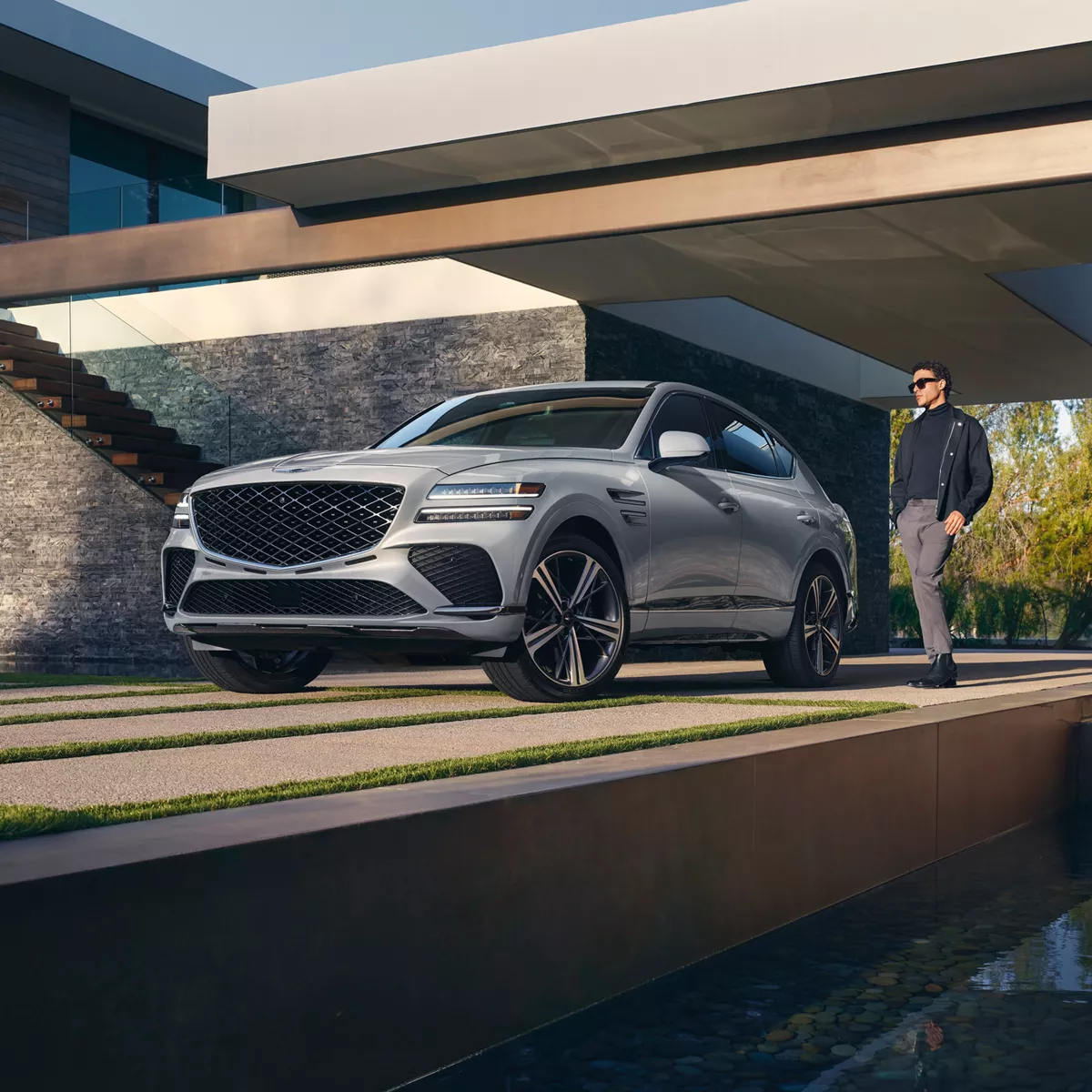3/4 front driver side view of Genesis GV80 Coupe in Bering Blue parked in carport of modern home