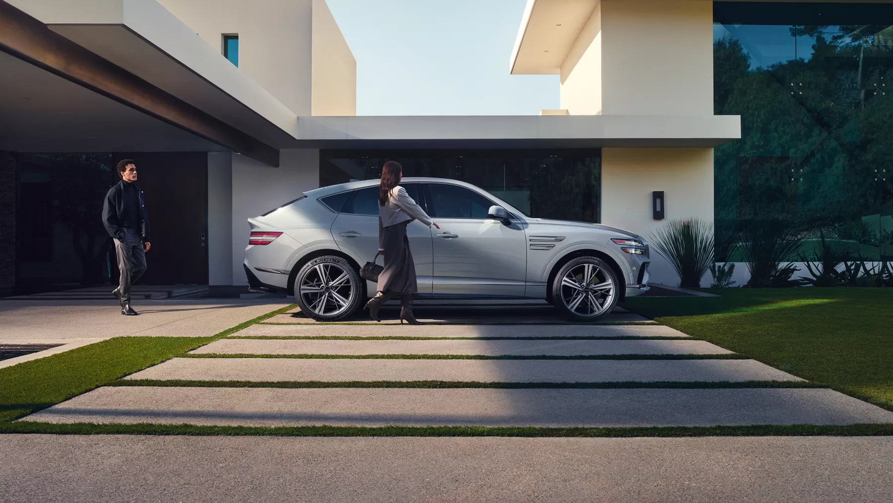 Passenger side profile view of Genesis GV80 Coupe in Bering Blue parked at a modern style home