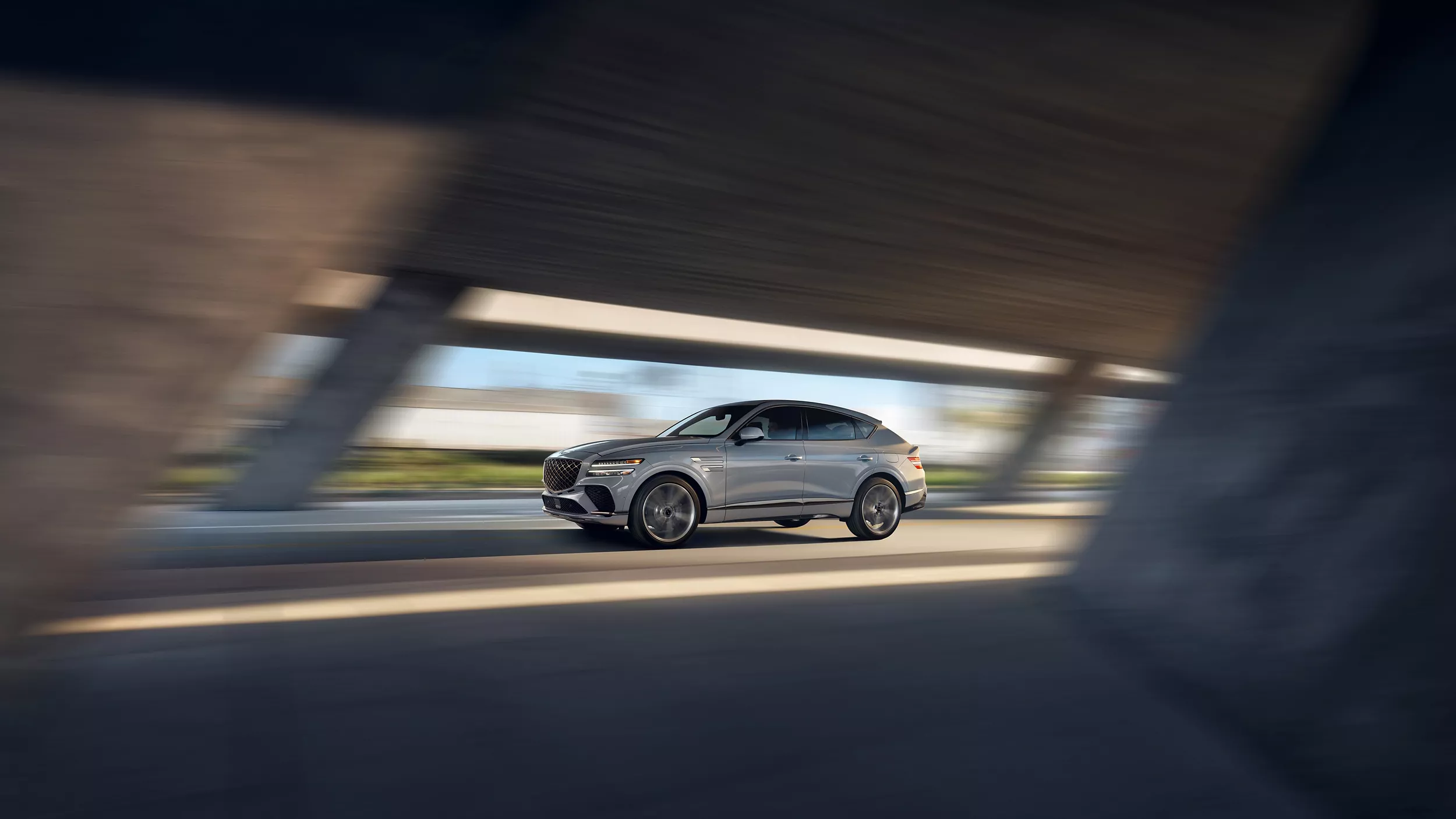 Driver side shot of Genesis GV80 Coupe in Bering Blue driving through bridge/tunnel