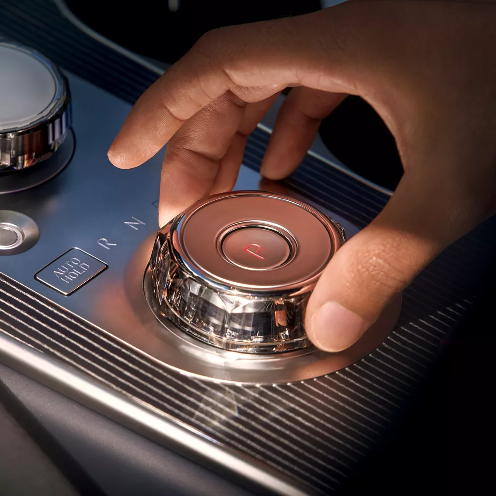 Interior closeup of hand using shift-by-wire knob on center console inside Genesis GV80 Coupe