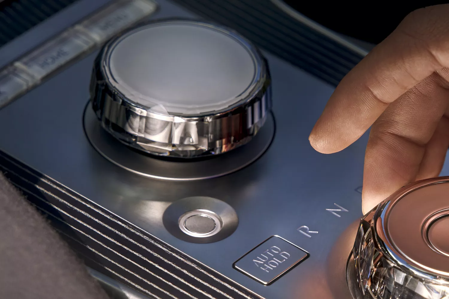 Interior closeup of hand reaching shift-by-wire knob on center console inside Genesis GV80 Coupe