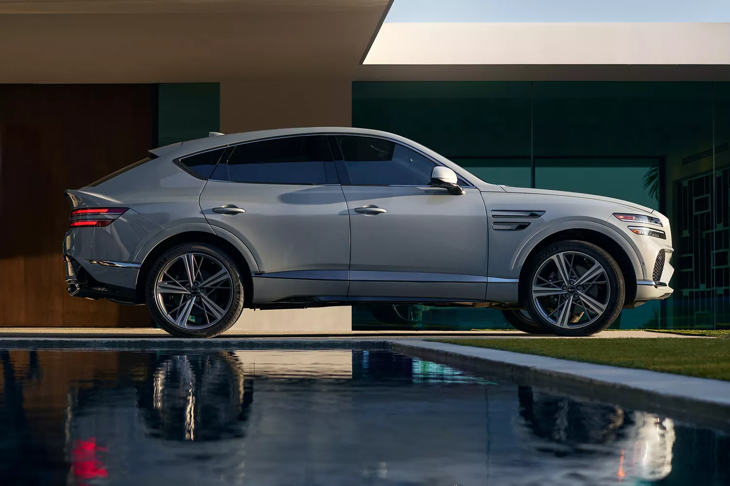 Genesis GV80 Coupe in modern setting with two people walking beside it reflected in a pool of water
