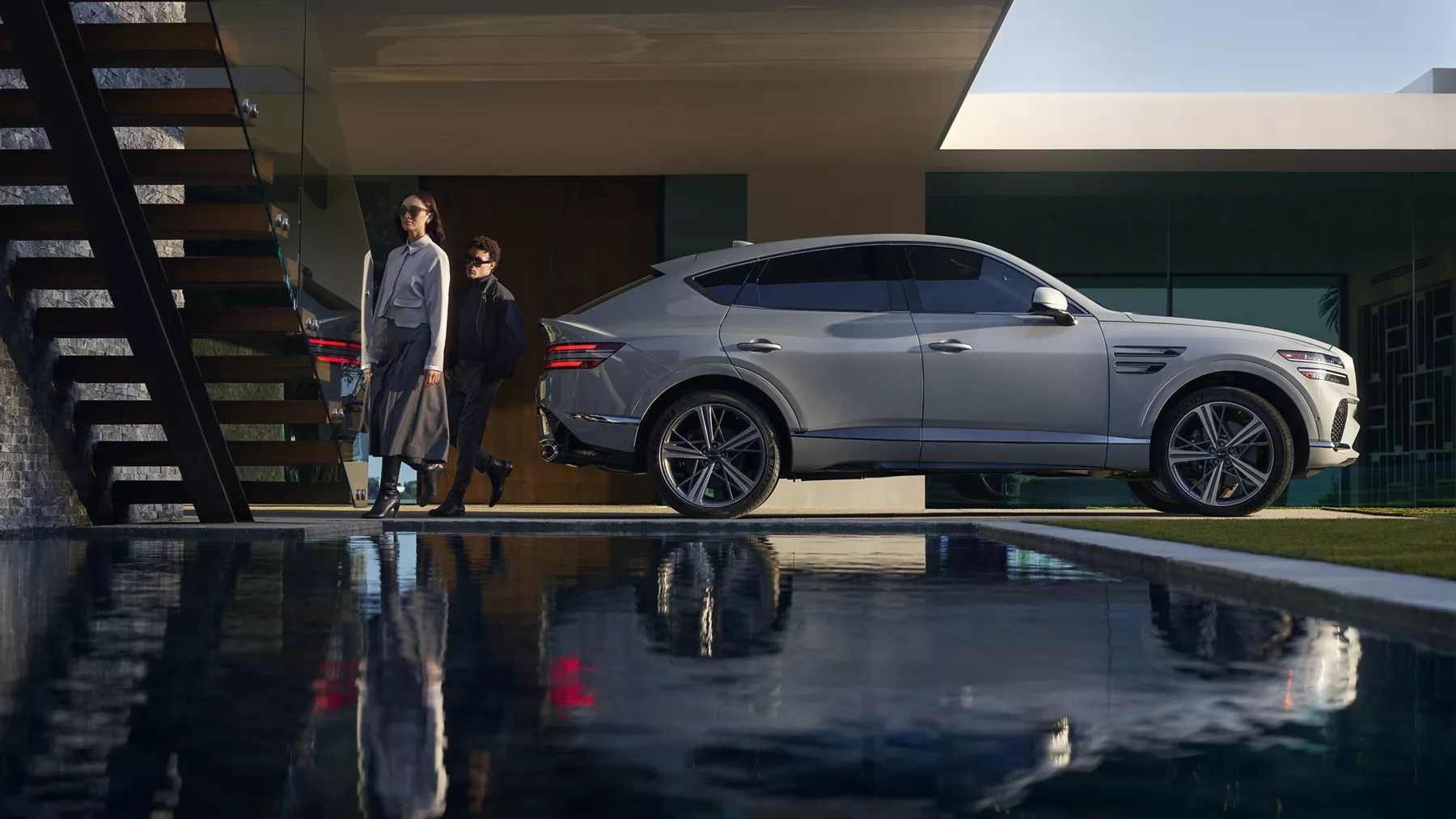 Genesis GV80 Coupe in modern setting with two people walking beside it reflected in a pool of water