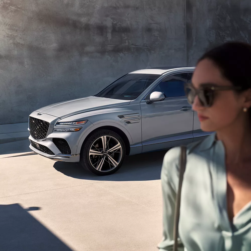 3/4 front driver side image of Genesis GV80 Coupe in Bering Blue, with woman in foreground
