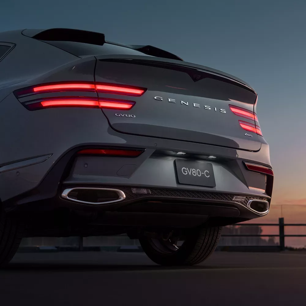 Rear view of Genesis GV80 Coupe in Bering Blue at sunset with illuminated taillights