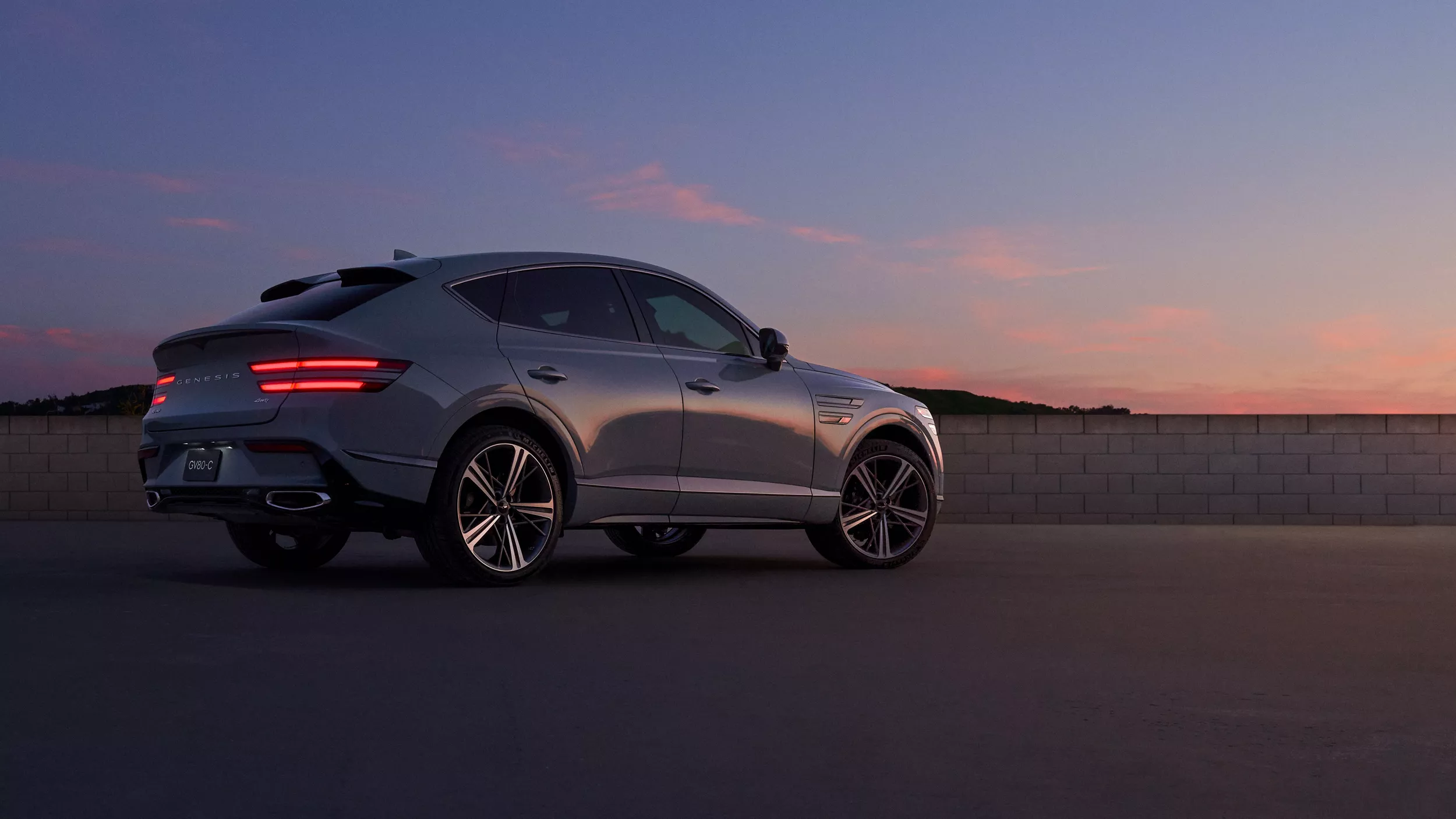 7/8 rear passenger side view of Genesis GV80 Coupe in Bering Blue parked during a desert sunset