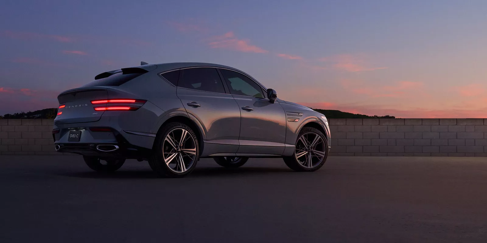 7/8 rear passenger side view of Genesis GV80 Coupe in Bering Blue parked during a desert sunset