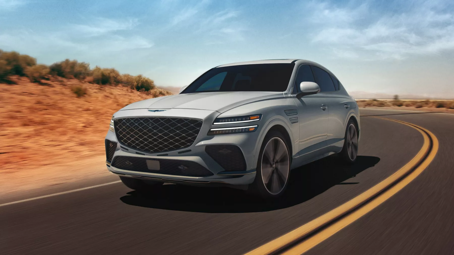 Front 3/4 driver side shot of Genesis GV80 Coupe in Bering Blue driving along curved desert road