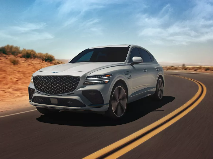 Front 3/4 driver side shot of Genesis GV80 Coupe in Bering Blue driving along curved desert road