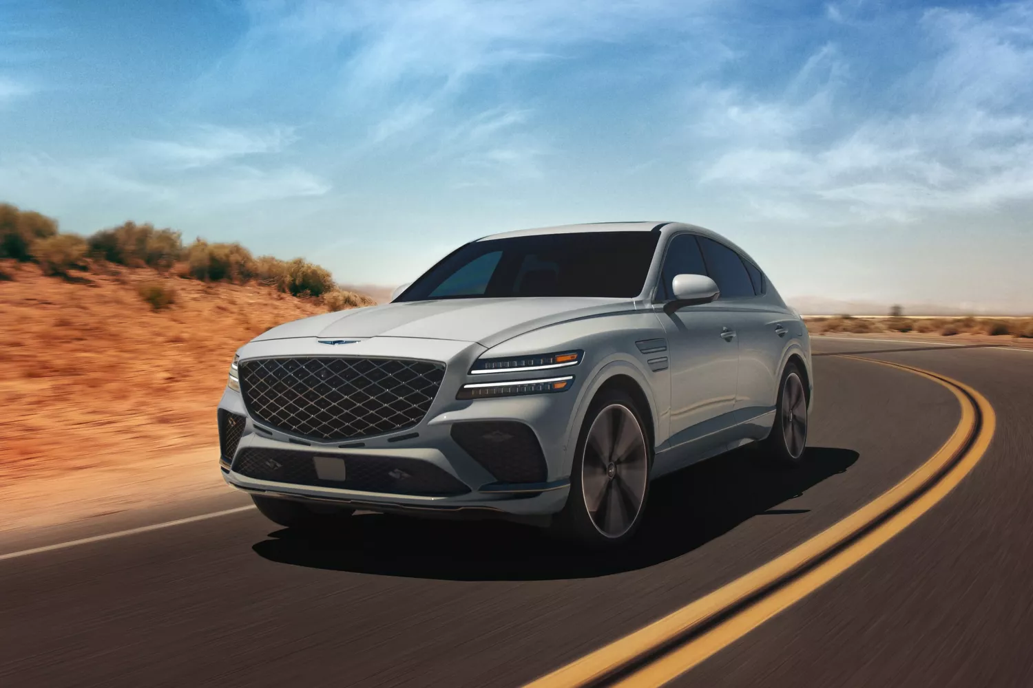 Front 3/4 driver side shot of Genesis GV80 Coupe in Bering Blue driving along curved desert road