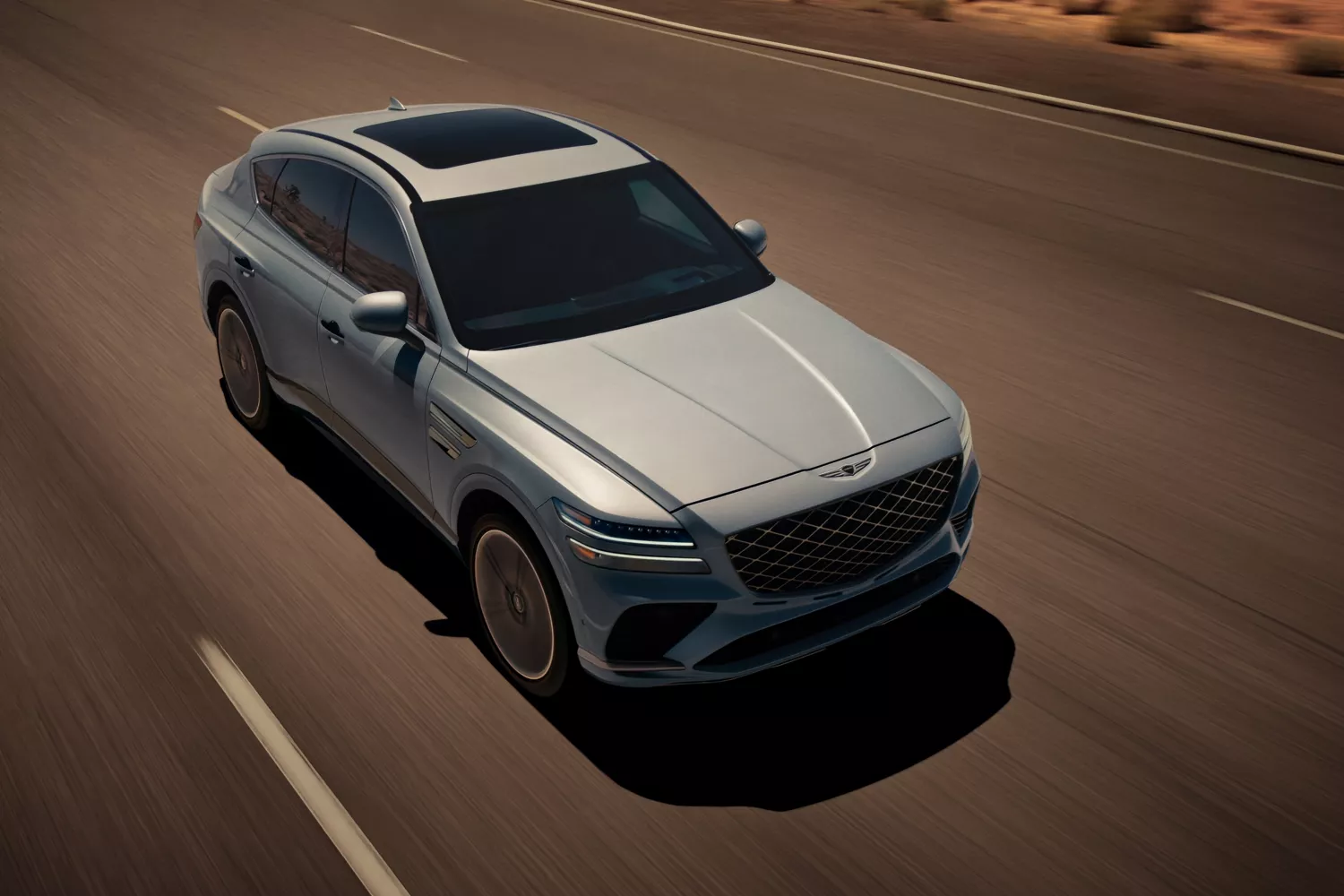 Overhead 7/8 front passenger side view of Genesis GV80 Coupe in Bering Blue driving on desert road