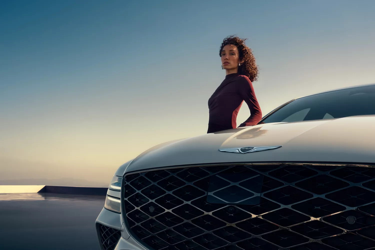 Low angle close up of Genesis G80 with woman leaning against passanger door, sky in the background