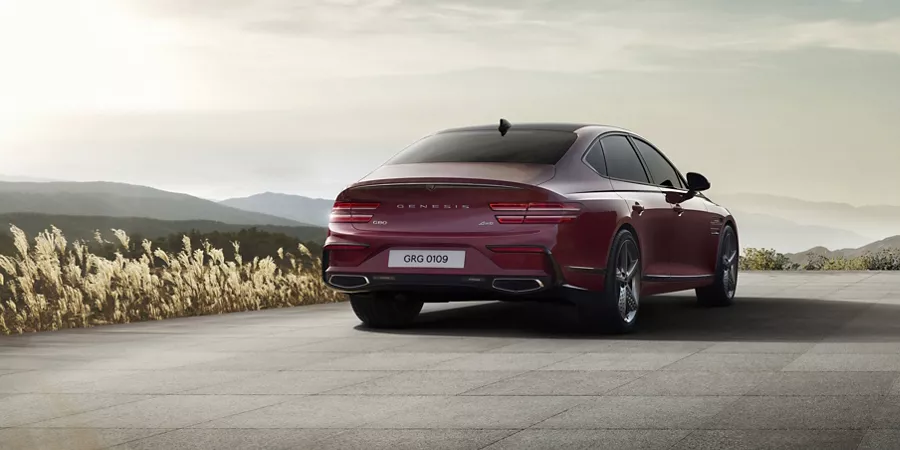 3/4 rear passenger side angle of Genesis G80 in Cavendish Red driving down a road