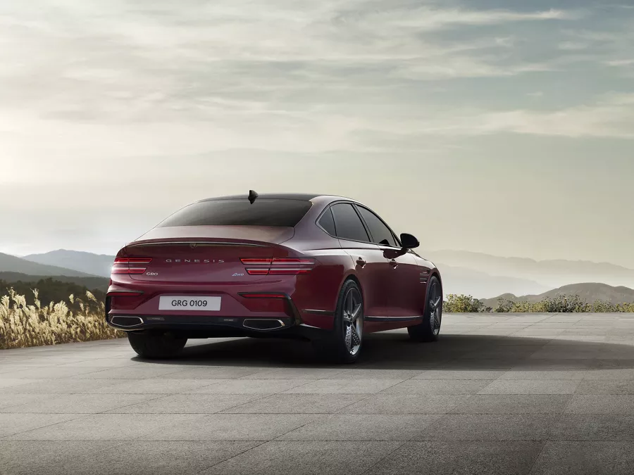 3/4 rear passenger side angle of Genesis G80 in Cavendish Red driving down a road